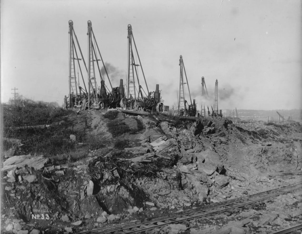 Steam operated drills boring holes for dynamite.
