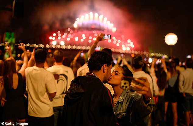 SYDNEY, AUSTRALIA - DECEMBER 31: People kiss as they enjoy the New Year's Eve firework displays at Opera House on December 31, 2025 in Sydney, Australia. Thousands turned out to celebrate New Year's Eve in Sydney, as the Harbour Bridge lit up with fireworks. (Photo by George Chan/Getty Images)