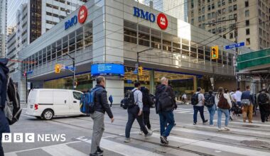 People on a crosswak on King Street in Toronto, a major intersection. In  the background is a grey building with a sign reading 'BMO'