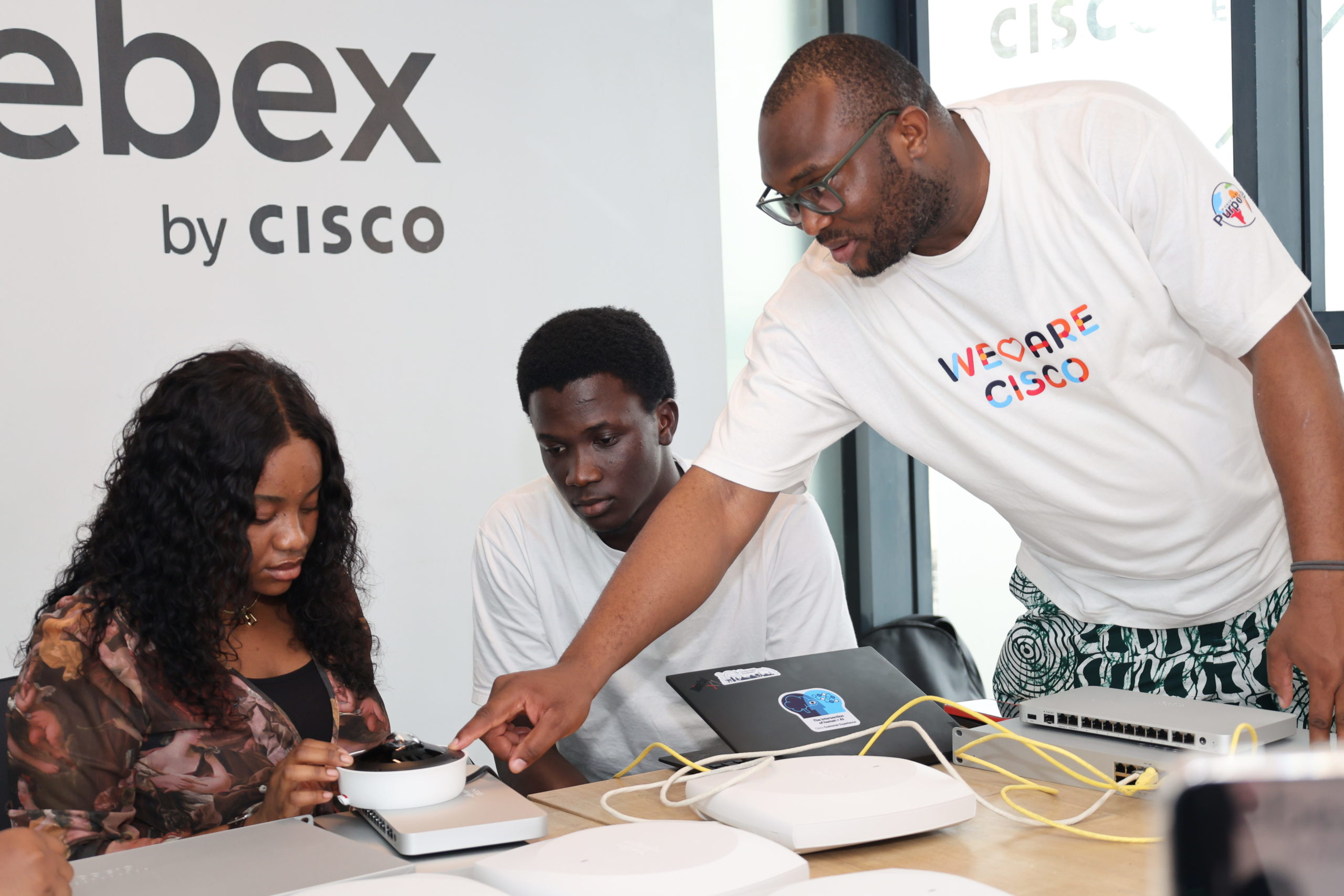 Man helping two people sitting at a table with devices.