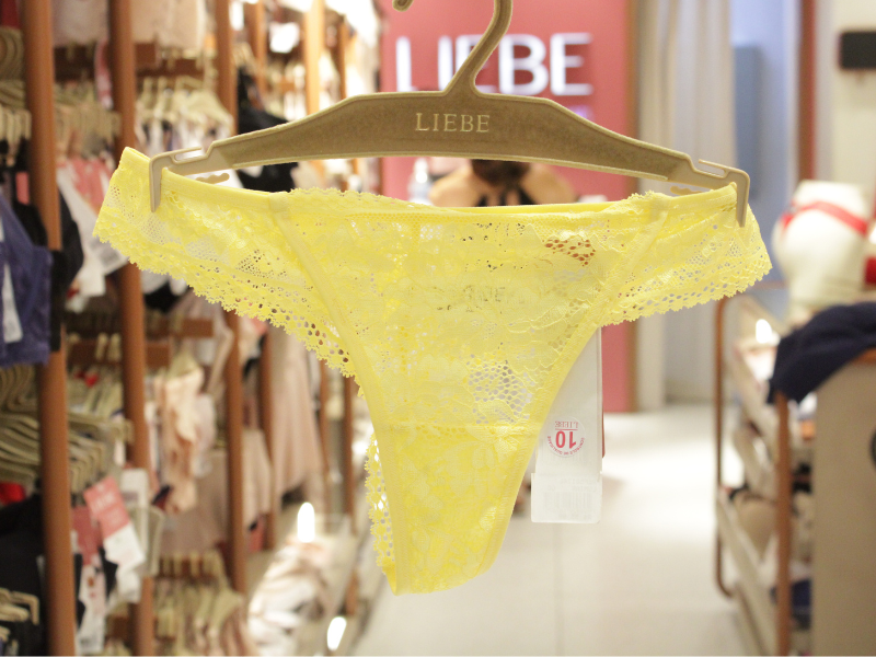 Calcinha de renda amarela vibrante pendurada em um cabide da marca Liebe, com detalhes delicados nas bordas.