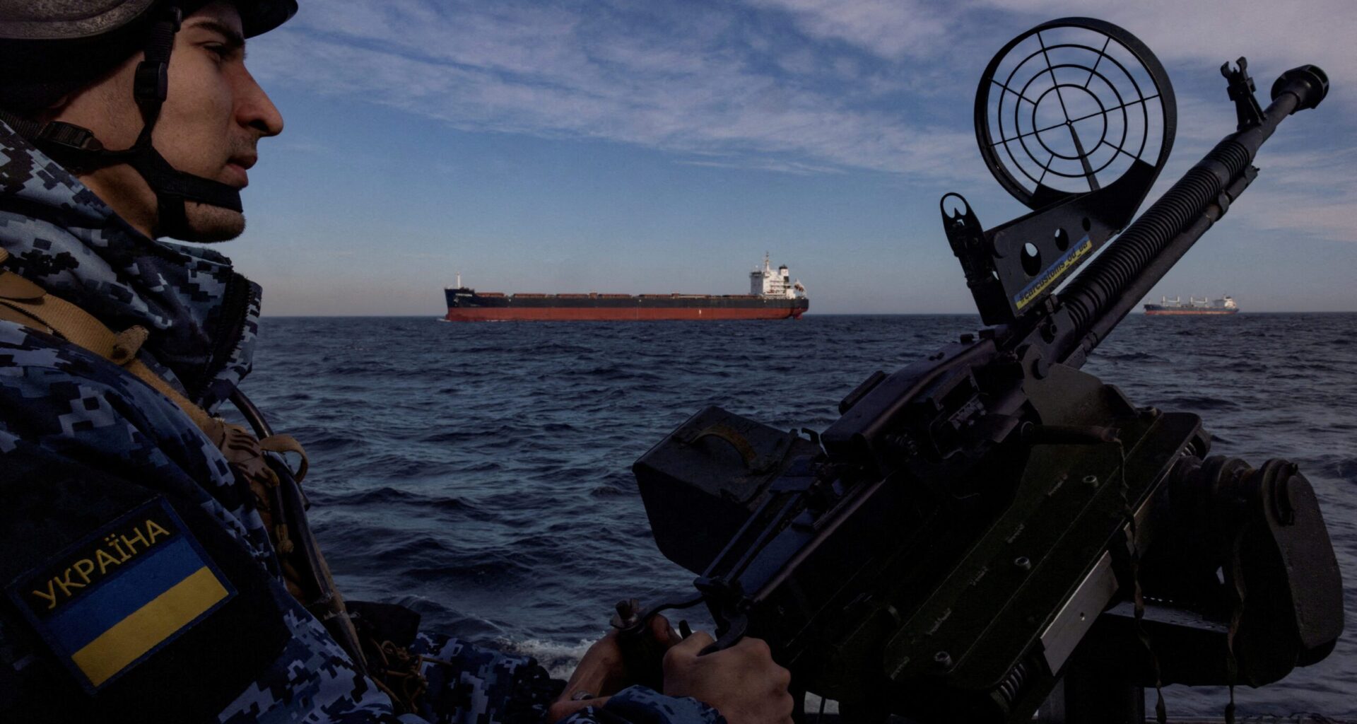 Ukraine coast guardsman manning a deck gun with an oil tanker in the background
