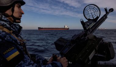 Ukraine coast guardsman manning a deck gun with an oil tanker in the background
