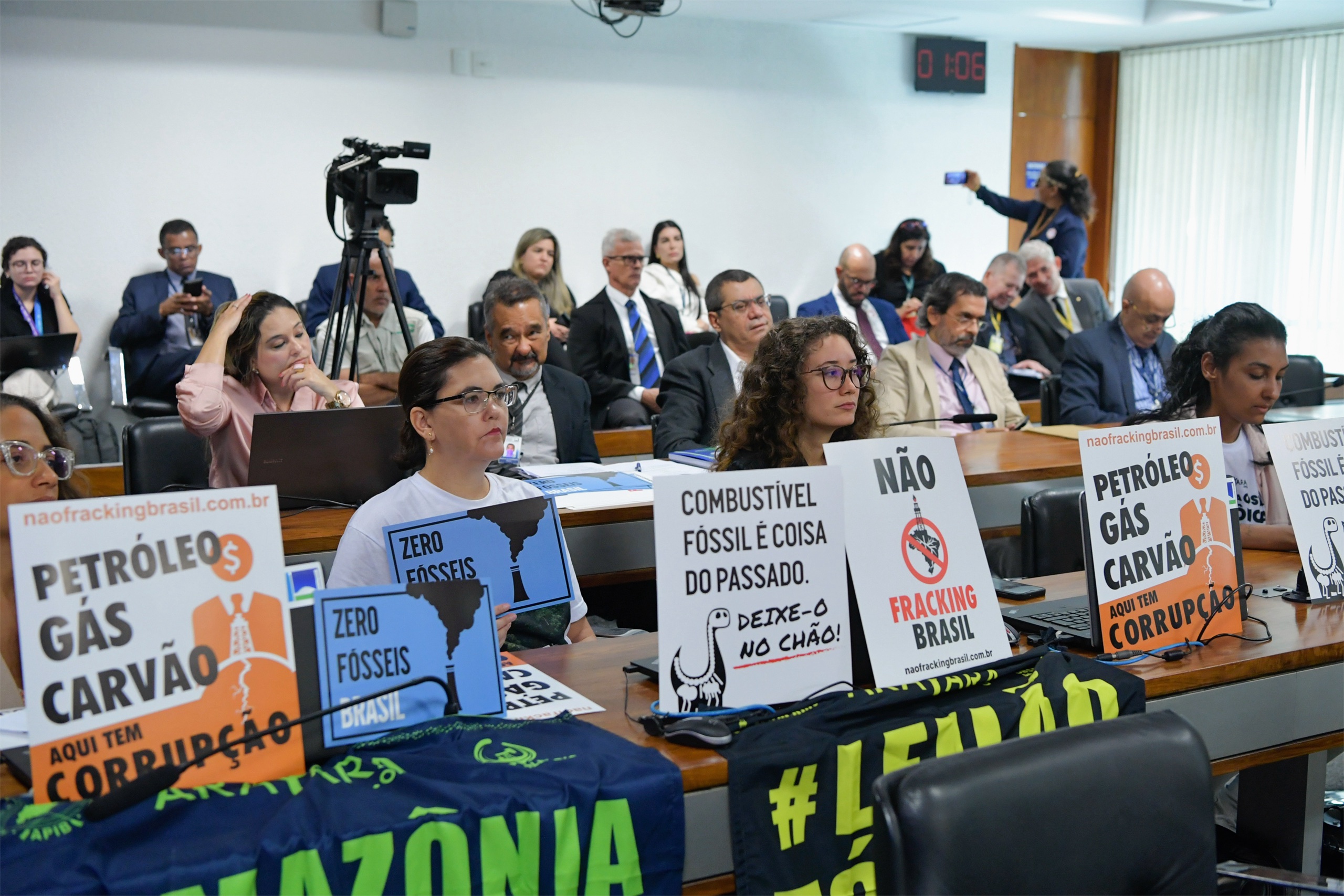 A meeting room filled with attendees holding signs opposing fossil fuels and fracking