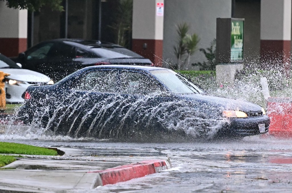 A car drives through a flooded street, kicking up large splashes of water.