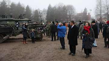 Ihmisiä tarkastelemassa sotilasajoneuvoa ulkotapahtumassa talvisessa säässä. Panssarivaunun edessä perhe poseeraa.