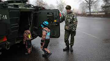 Sotilas pitää armeijan ajoneuvon ovea auki ja kksi lasta menee sisälle.