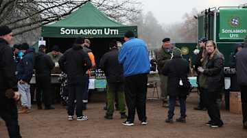 Ihmisiä jonottamassa vihreän teltan edessä. Teltassa lukee Sotilaskoti Utti. Taustalla sumuinen maisema.
