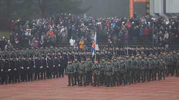 Sotilaita kentällä järjestäytyneenä. Taustalla katsomossa yleisöä. Sää on sumuinen.