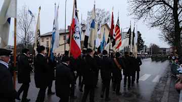 Lipunkantajat marssivat kadulla Suomen itsenäisyyspäivän juhlakulkueessa. Kadun varrella paljon katsojia.