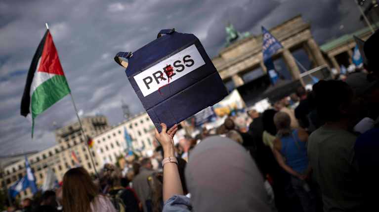 Mielenosoittaja nostaa kylttiä, jossa press-tekstin päällä on punaista symboloimassa verta.