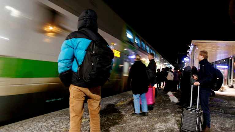 People standing on a platform as a train arrives at the station in the evening.