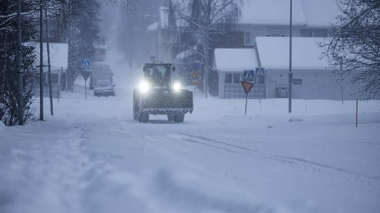A large snow removal vehicle driving down a snowy suburban road.