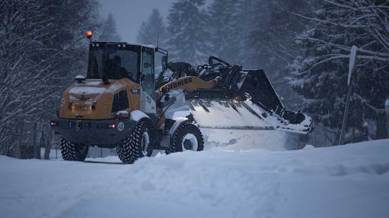 Tractor clearing snow from a road with forest in the background.