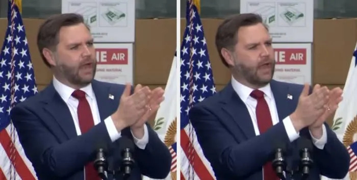 Man in a suit speaking at a podium with U.S. flags in the background
