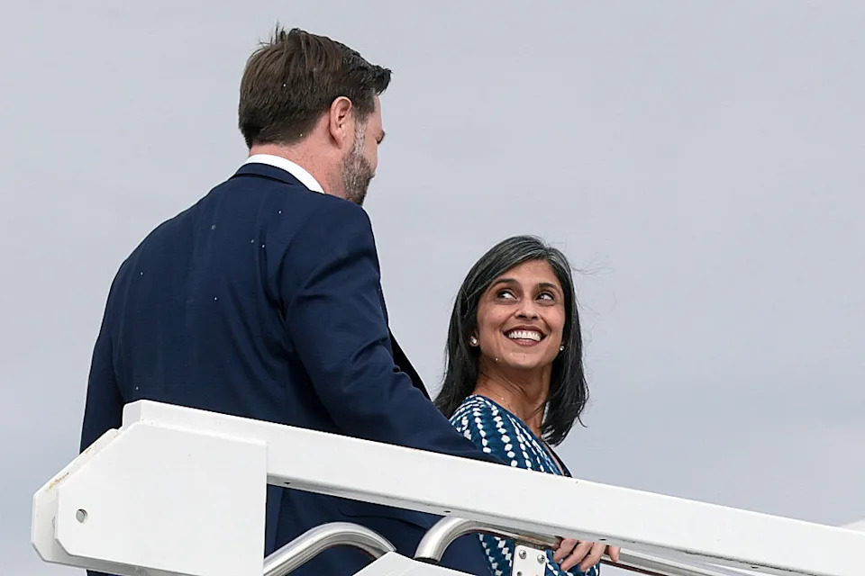 usha vance in a patterned dress smiles while exiting a plane with jd vance in a suit