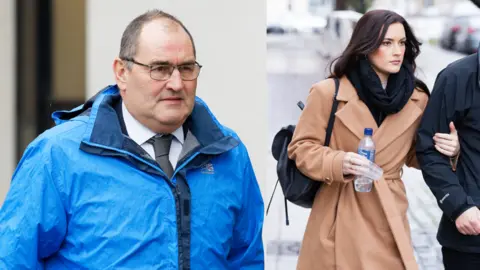 Athena Pictures Agency A man is wearing glasses while walking in a bright blue rain coat, wearing a grey tie and white shirt. A woman is clutching a person's upper arm while walking and holding a water bottle. She is wearing a beige coloured coat and a black scarf.