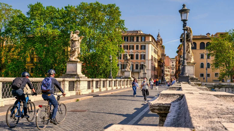 two people on bikes crossing a bridge in rome