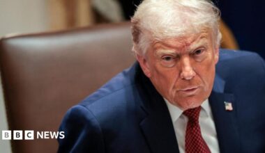 Donald Trump frowning in a navy suit with a white shirt and red tie