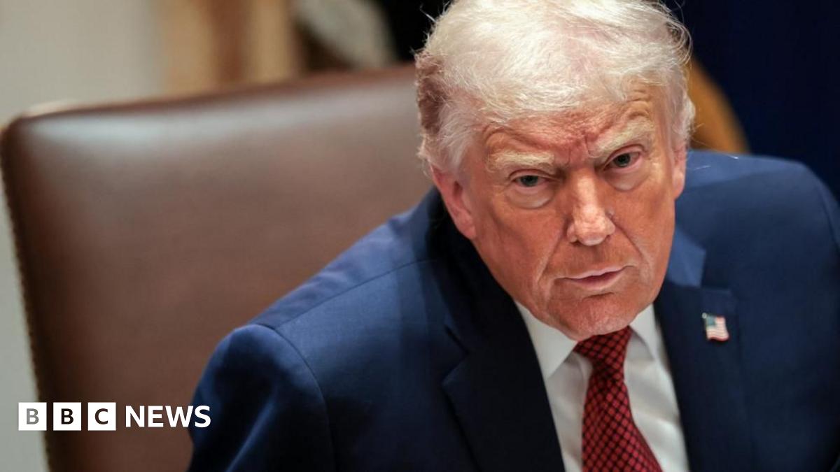 Donald Trump frowning in a navy suit with a white shirt and red tie