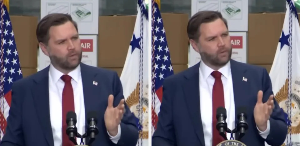 A man in a suit speaks at a podium with flags in the background