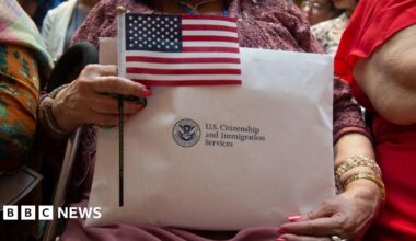 A woman holding her citizenship papers from US Citizenship and Immigration Services, along with a small American flag, while waiting to take her oath
