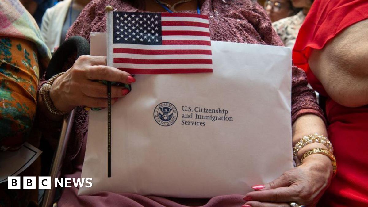A woman holding her citizenship papers from US Citizenship and Immigration Services, along with a small American flag, while waiting to take her oath