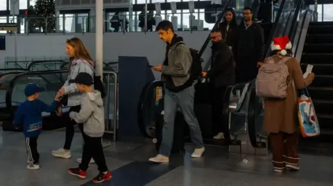 EPA People coming down an escalator at an airport as a person in a Santa hat goes up the other side