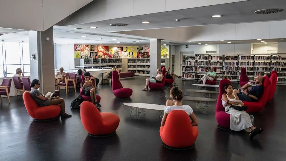 About a dozen people are seen sitting or reading on chairs in a library during a heatwave in Barcelona