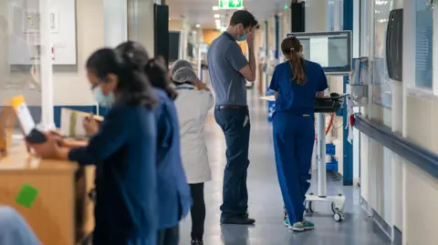 PA Media People wearing blue hospital clothing stand in a hospital corridor.