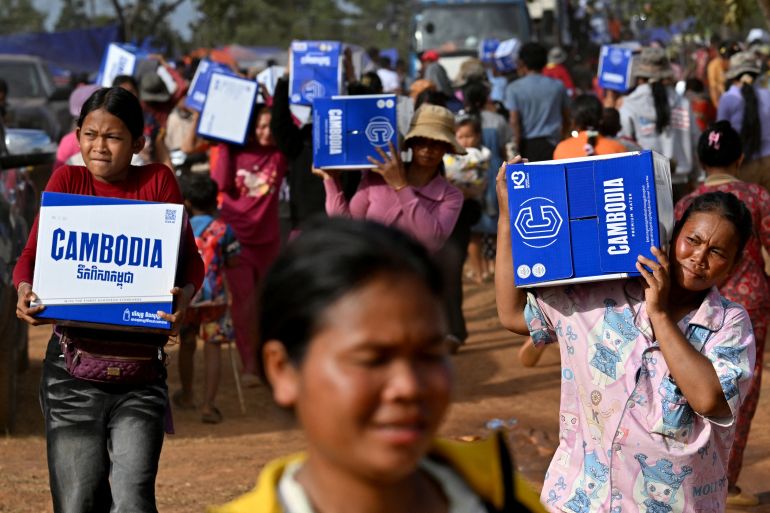 Displaced people carry boxes with drinking water distributed at a temporary camp in Cambodia's Oddar Meanchey province on December 11, 2025, amid clashes along the Cambodia-Thailand border. Renewed fighting raged at the border of Cambodia and Thailand on December 11, with combat heard near centuries-old temples, ahead of an expected phone call from US President Donald Trump to the two nations' leaders. (Photo by TANG CHHIN Sothy / AFP)