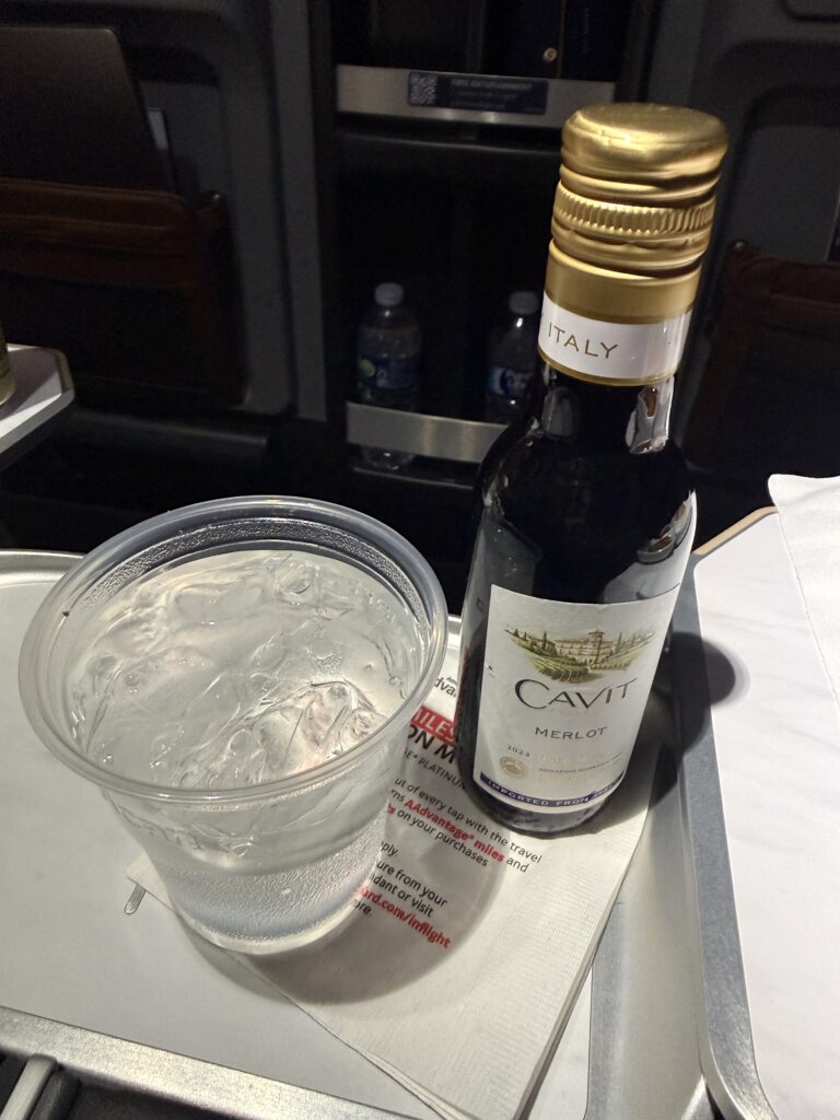 A mini bottle of wine and a glass of sparkling water sit on the cocktail table. 
