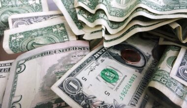 A close-up of assorted U.S. dollar bills and coins, including one- and five-dollar notes, scattered and partially stacked.
