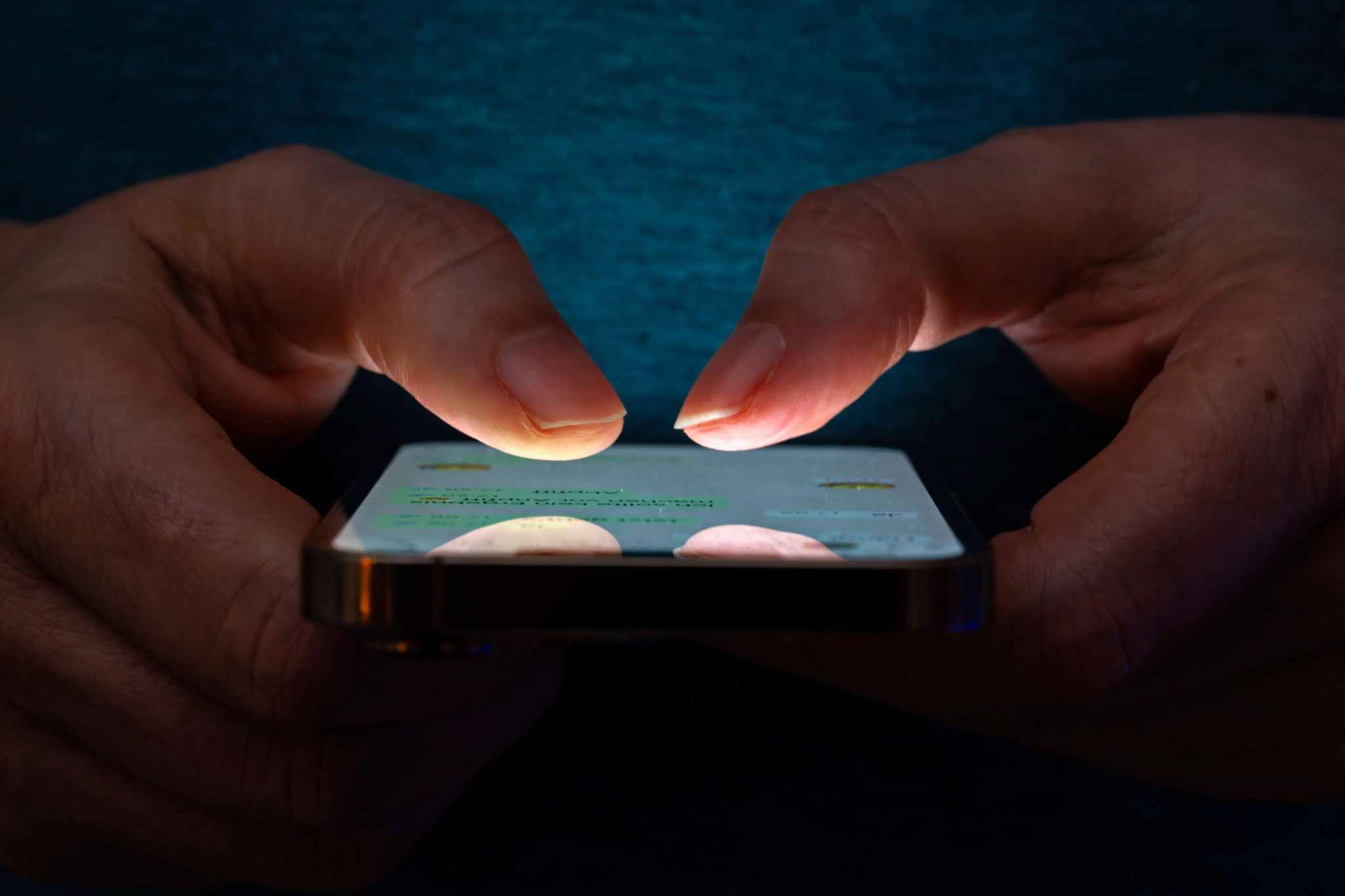 Frau tippt SMS auf Apple iPhone13 in schlechter Beleuchtung, Hände und Smartphone-Bildschirm hervorgehoben.