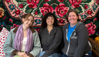WSU students Cecilia Sevier, Mackenzie Aragon, and Julie Hilland posing for a group photo beneath a floral wall hanging.