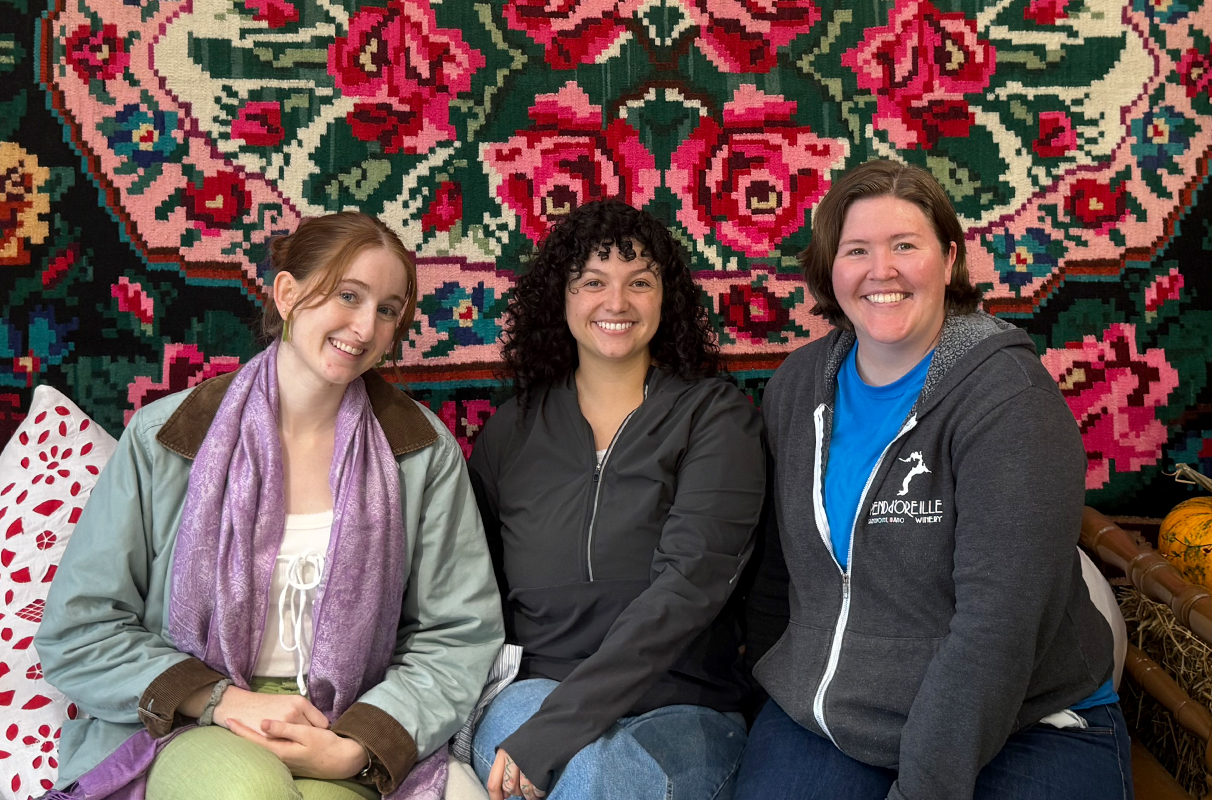 WSU students Cecilia Sevier, Mackenzie Aragon, and Julie Hilland posing for a group photo beneath a floral wall hanging.