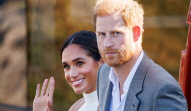 Meghan Markle wears a white halter top and waves while Prince Harry, who has red hair, wears a gray suit jacket and white shirt
