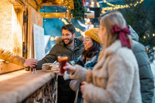Friends Enjoying Mulled Wine at Holiday Market Counter with Festive Lights