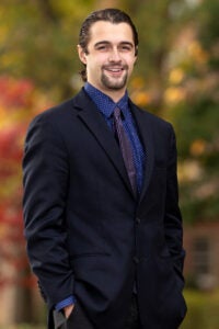A young man wearing a suit stands with his hands in his pockets.