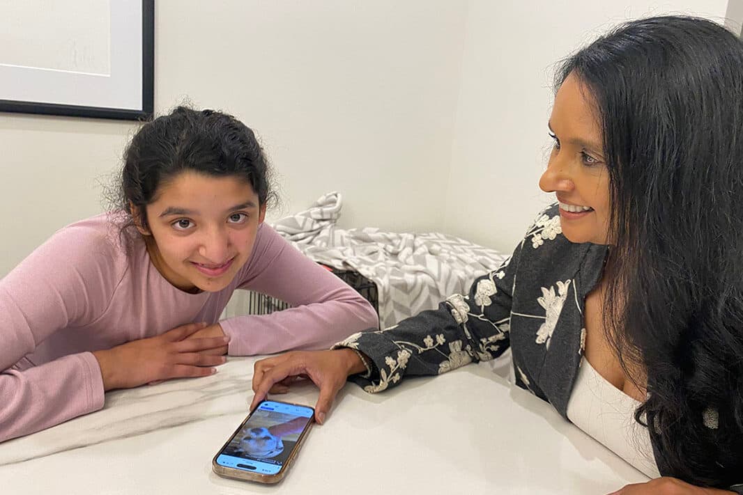 Two women are sitting at a table, with one of them holding a cell phone. They are discussing the content displayed on the phone screen.