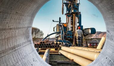 Metal tubes stacked near an oil and gas drilling platform.