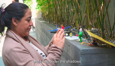 person holds phone up while creating video using small toys, subtitle reads 'and living under the shadows.'