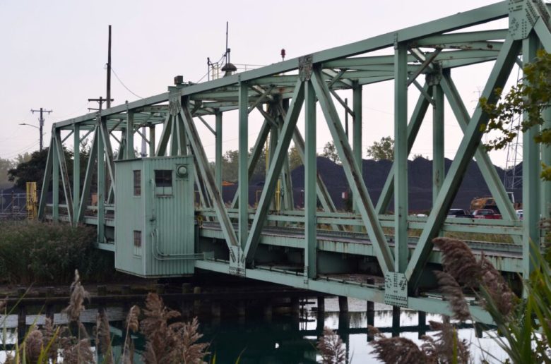 A green swing bridge on the west side of industrialized Zug Island
