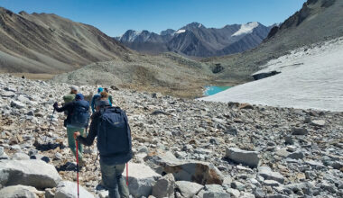 Människor vandrar i en dalgång intill ett vattendrag med berg i bakgrunden.