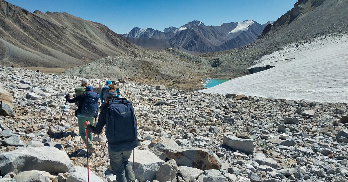 Människor vandrar i en dalgång intill ett vattendrag med berg i bakgrunden.