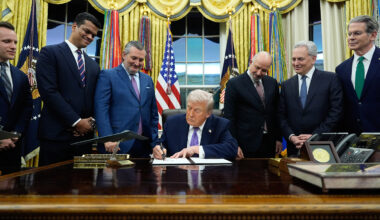 Trump sign's an executive order in the oval office with a group of men of suits standing around him.