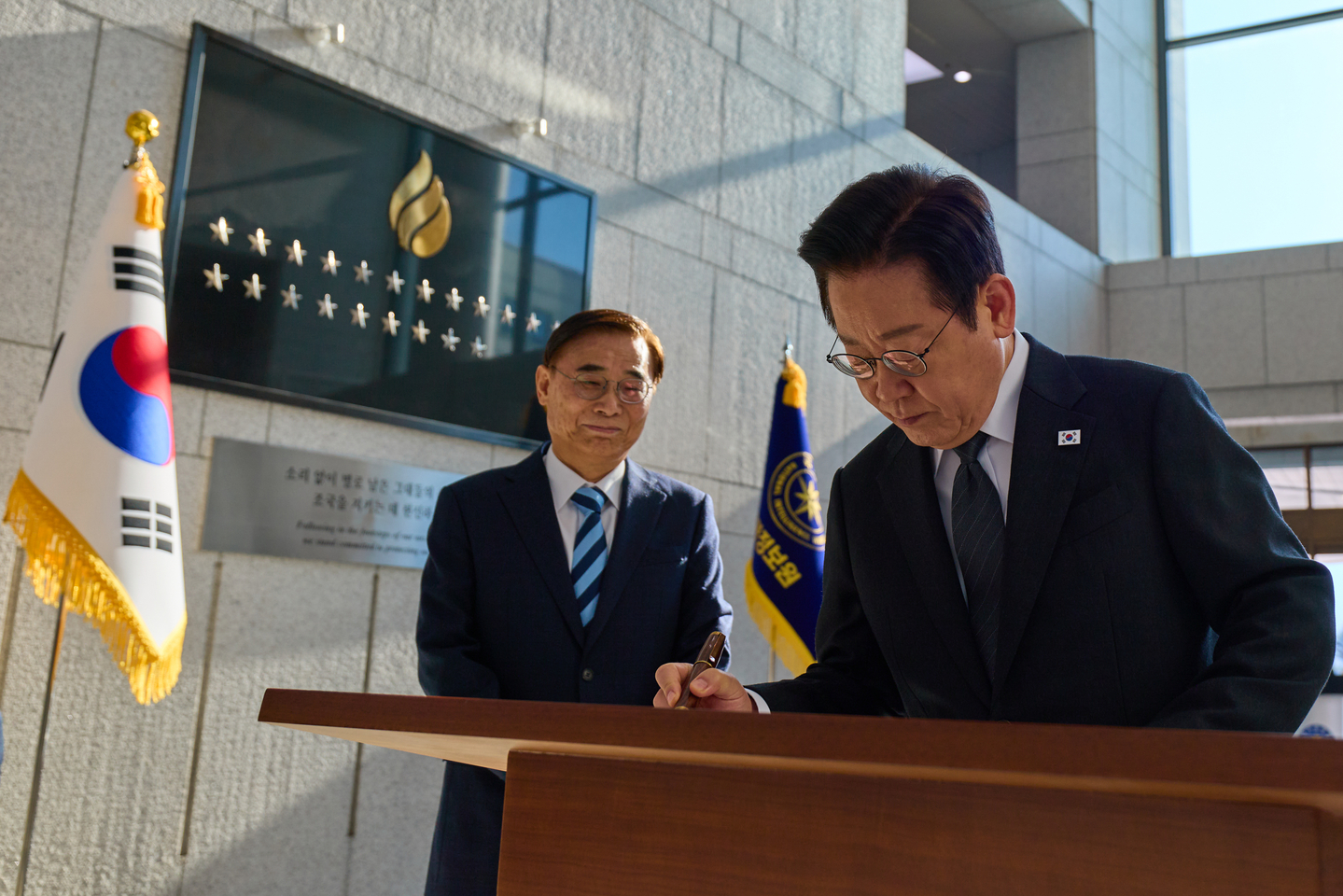 President Lee Jae Myung, right, signs a guestbook during his first visit as president to the National Intelligence Service on Nov. 28. [NEWS1]