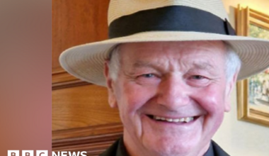 Philip Gosling smiling and wearing a straw hat. He also has on a black suit and white tie.