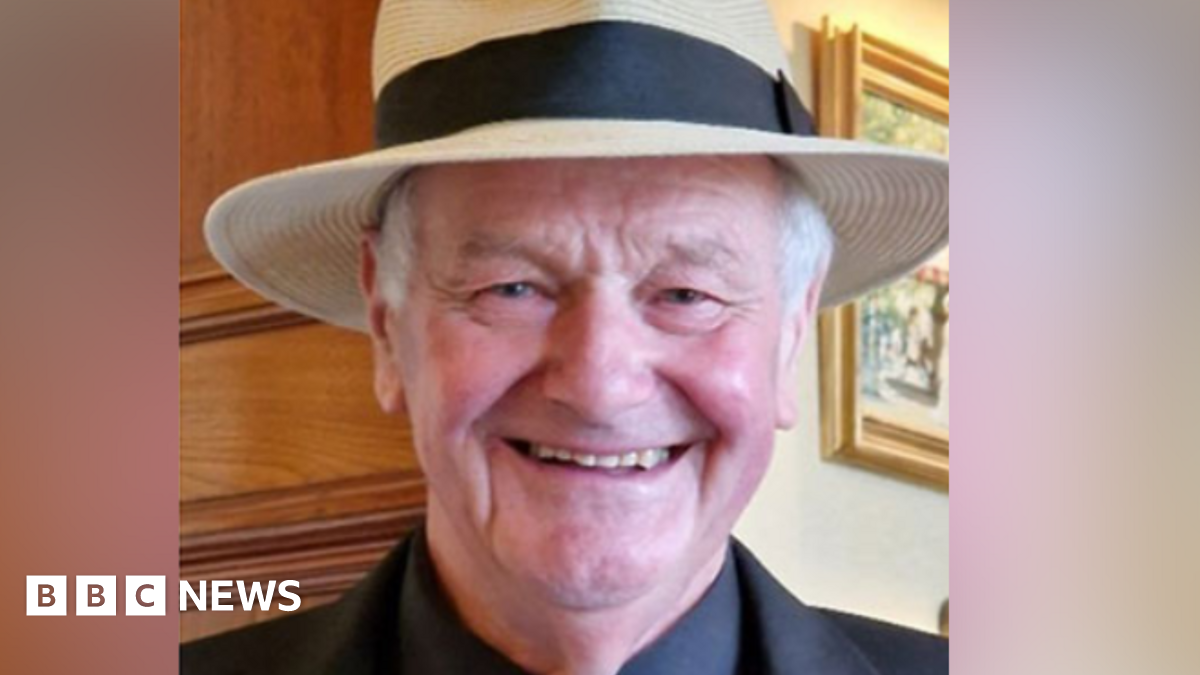 Philip Gosling smiling and wearing a straw hat. He also has on a black suit and white tie.
