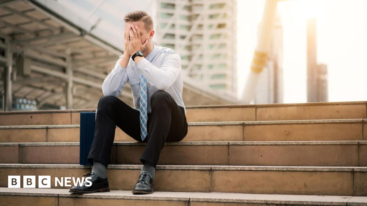 A man in office clothes sits on some steps. He looks bereft of hope.
